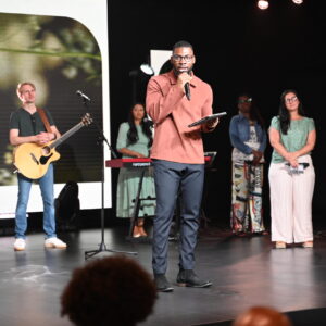 A young man speaks on stage, encouraging young adults to grow in their faith, follow Jesus, and live out God’s purpose in their lives.
