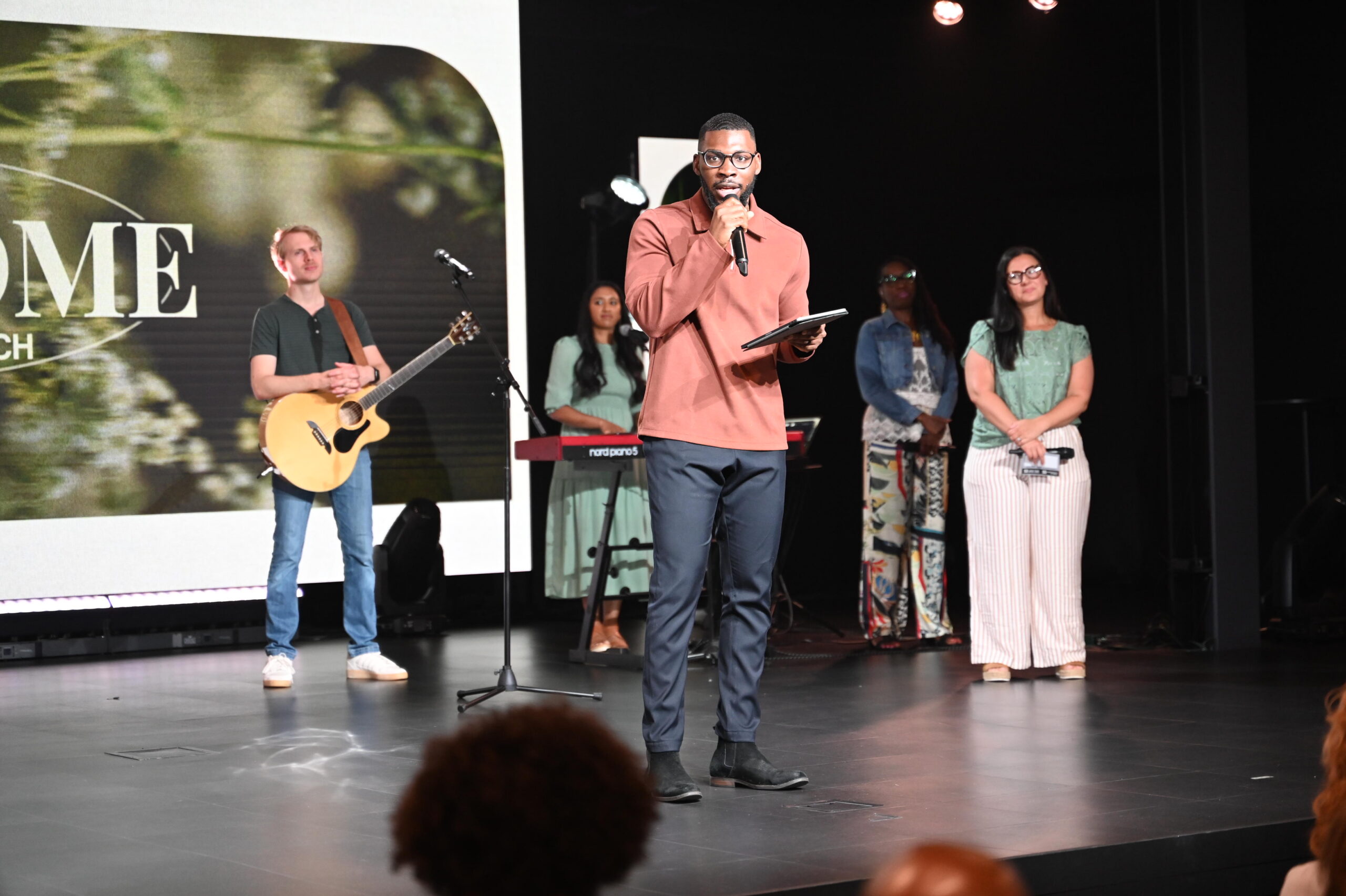 A Young Man Speaks On Stage, Encouraging Young Adults To Grow In Their Faith, Follow Jesus, And Live Out God’s Purpose In Their Lives.